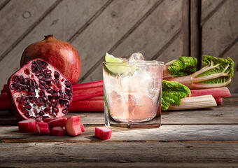 Ett rosa cocktailglas med rabarber och granatäpple bredvid 